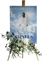 A personalized memorial or celebration poster displayed on a wooden easel, decorated with a floral arrangement in the foreground. The poster features a portrait of a man in a white outfit against a blue sky with clouds and doves, with the text 'CELEBRATING' and 'with Justin SMALLS'.